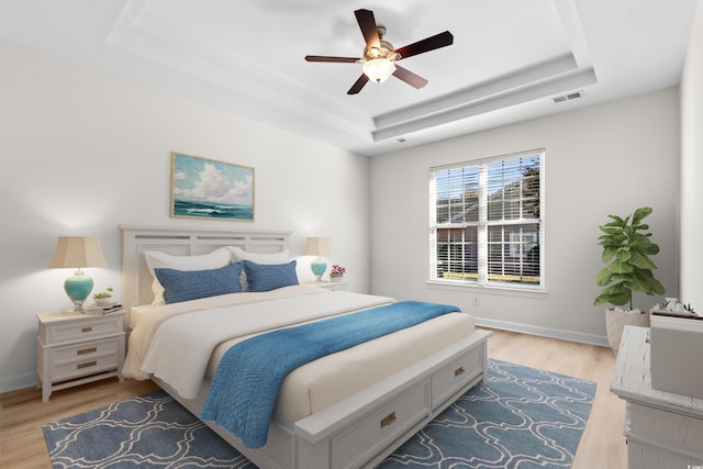 bedroom with ceiling fan, a raised ceiling, and light hardwood / wood-style floors