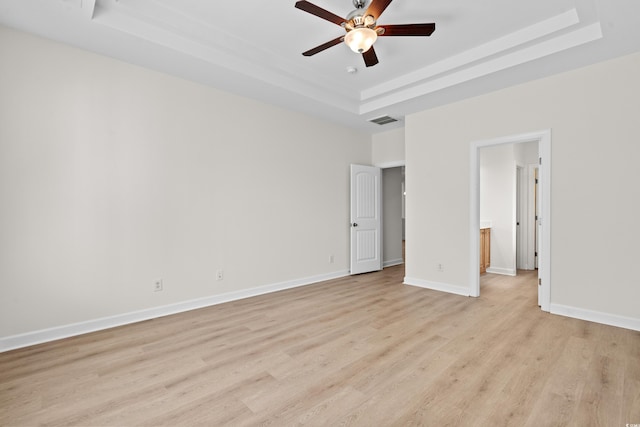 unfurnished bedroom with ceiling fan, ensuite bathroom, a tray ceiling, and light wood-type flooring