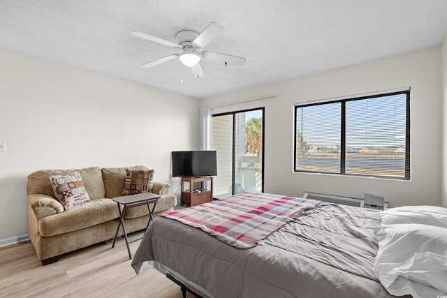 bedroom with ceiling fan, light hardwood / wood-style floors, a textured ceiling, and access to outside