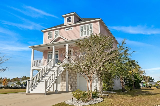 raised beach house with covered porch, a front yard, and a garage