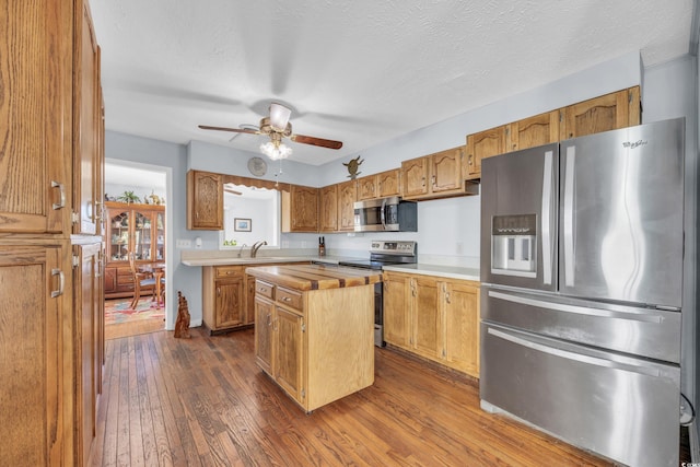 kitchen featuring appliances with stainless steel finishes, a textured ceiling, ceiling fan, dark wood-type flooring, and a kitchen island