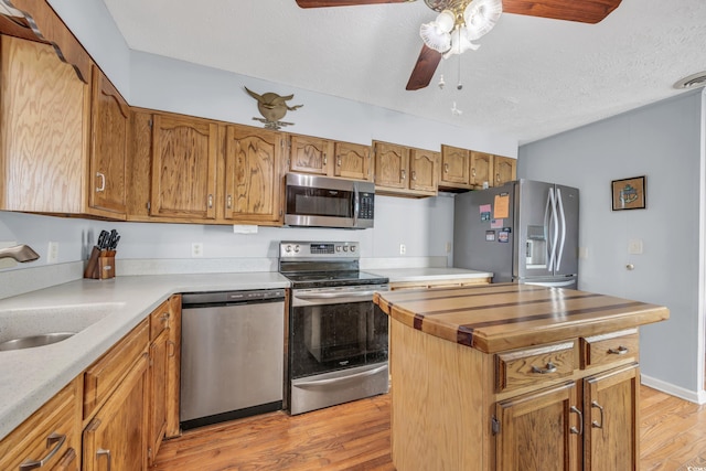 kitchen featuring ceiling fan, sink, a textured ceiling, appliances with stainless steel finishes, and light wood-type flooring