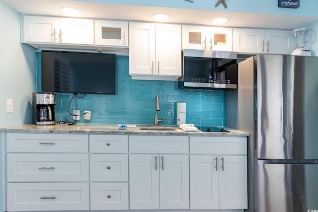 kitchen featuring white cabinetry, sink, stainless steel appliances, light stone counters, and decorative backsplash