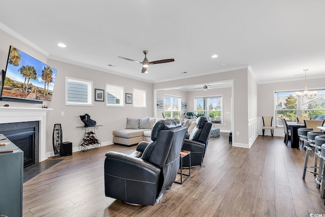 living room with ceiling fan with notable chandelier, a healthy amount of sunlight, wood-type flooring, and ornamental molding