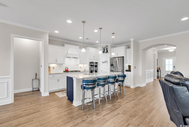 kitchen with custom exhaust hood, stainless steel appliances, pendant lighting, a center island with sink, and white cabinetry