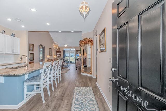 kitchen featuring a kitchen bar, white cabinetry, pendant lighting, and light stone countertops