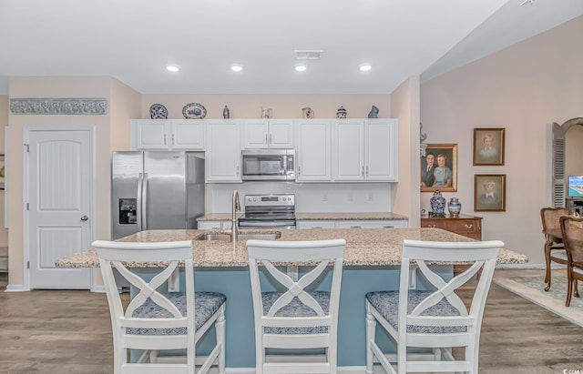 kitchen with stainless steel appliances, a center island with sink, white cabinets, and a breakfast bar