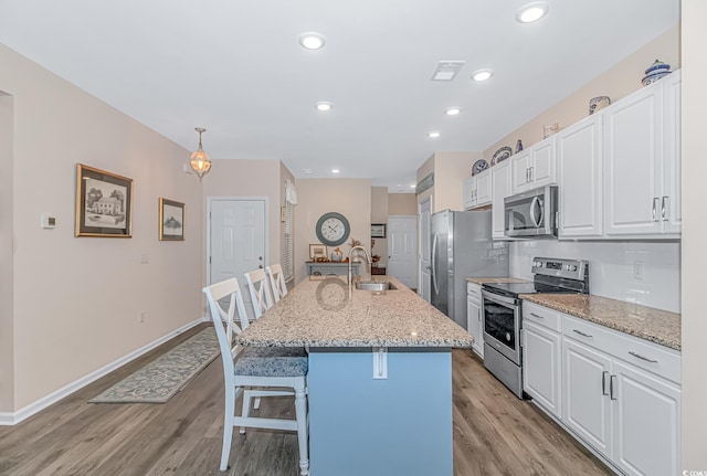 kitchen with a kitchen breakfast bar, stainless steel appliances, an island with sink, pendant lighting, and white cabinets