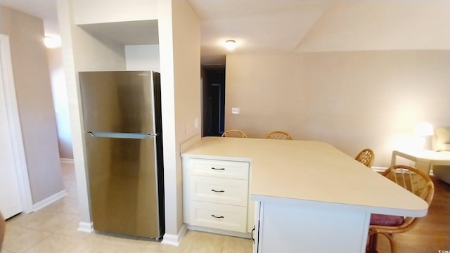 kitchen with a kitchen bar, stainless steel refrigerator, kitchen peninsula, and white cabinets