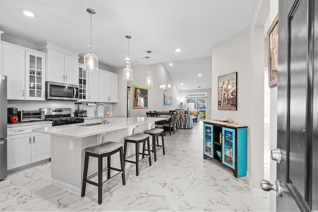 kitchen with light stone countertops, sink, stainless steel appliances, a center island with sink, and white cabinets