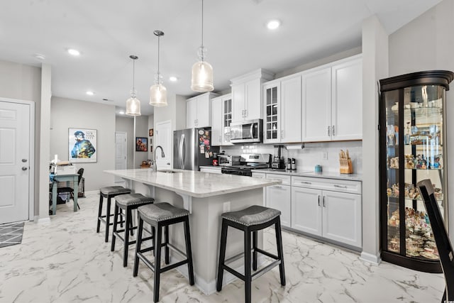 kitchen with stainless steel appliances, white cabinetry, hanging light fixtures, and a center island with sink