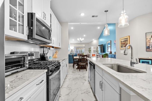 kitchen with pendant lighting, lofted ceiling, sink, appliances with stainless steel finishes, and white cabinetry