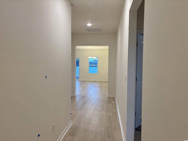 hall with light wood-type flooring and a notable chandelier