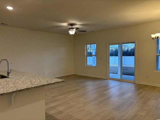 unfurnished living room with sink, light wood-type flooring, and ceiling fan with notable chandelier