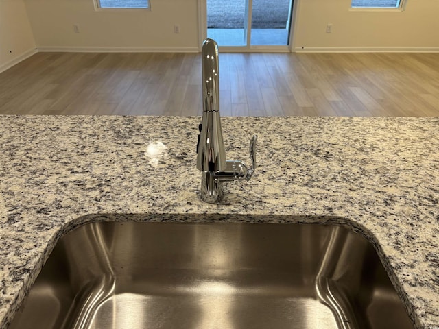 interior details with sink, hardwood / wood-style floors, and light stone counters