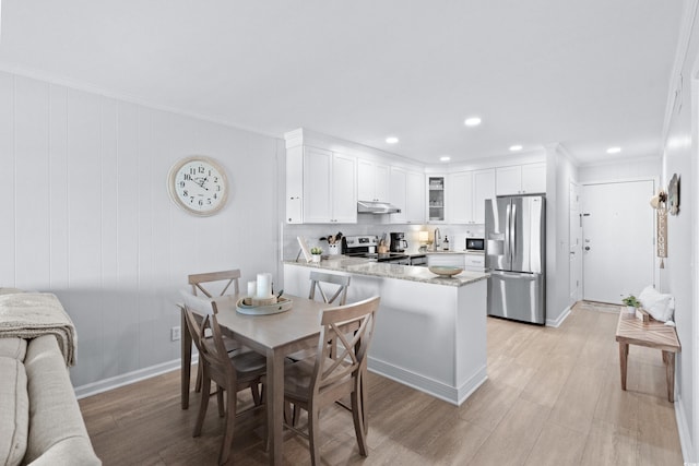 kitchen with stainless steel appliances, kitchen peninsula, crown molding, light hardwood / wood-style floors, and white cabinets