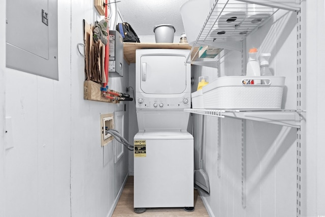 clothes washing area featuring light hardwood / wood-style flooring, a textured ceiling, electric panel, and stacked washer and clothes dryer