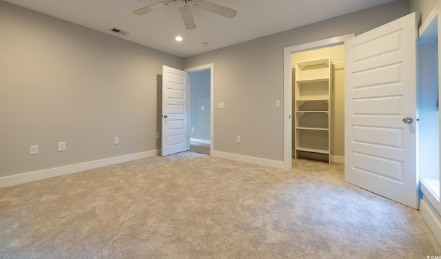 unfurnished bedroom with ceiling fan, light carpet, a walk in closet, and a closet