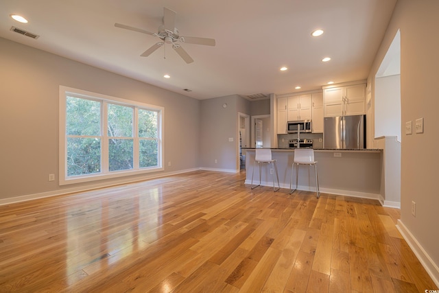 kitchen with kitchen peninsula, light hardwood / wood-style flooring, appliances with stainless steel finishes, white cabinets, and a kitchen breakfast bar