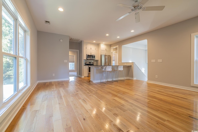 kitchen with appliances with stainless steel finishes, light hardwood / wood-style flooring, a kitchen breakfast bar, white cabinets, and kitchen peninsula