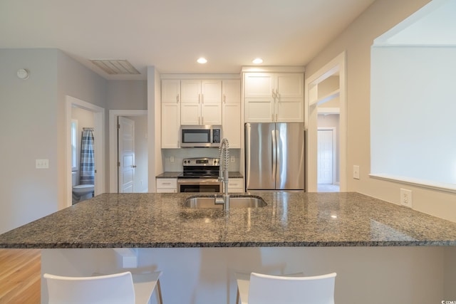 kitchen featuring dark stone countertops, appliances with stainless steel finishes, white cabinetry, and kitchen peninsula