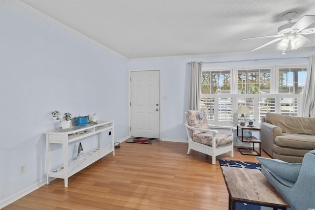 living area featuring a ceiling fan, light wood-style flooring, ornamental molding, and baseboards