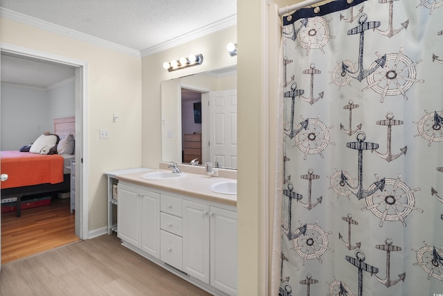 ensuite bathroom featuring a textured ceiling, a sink, wood finished floors, ornamental molding, and double vanity