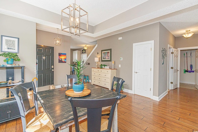 dining area with a textured ceiling, an inviting chandelier, and light hardwood / wood-style flooring