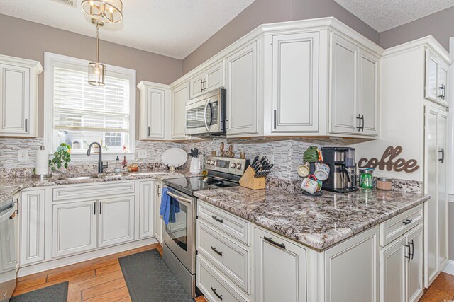 kitchen with white cabinetry, sink, hanging light fixtures, stainless steel appliances, and light hardwood / wood-style floors