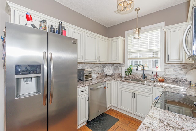 kitchen featuring appliances with stainless steel finishes, sink, light hardwood / wood-style flooring, white cabinets, and hanging light fixtures