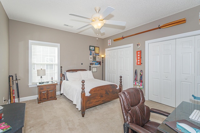 bedroom featuring a textured ceiling, ceiling fan, light colored carpet, and two closets