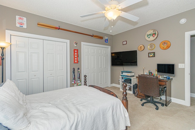 carpeted bedroom with ceiling fan, a textured ceiling, and multiple closets