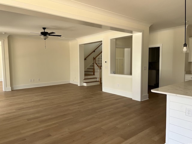 unfurnished living room featuring dark wood-style floors, crown molding, a ceiling fan, baseboards, and stairs