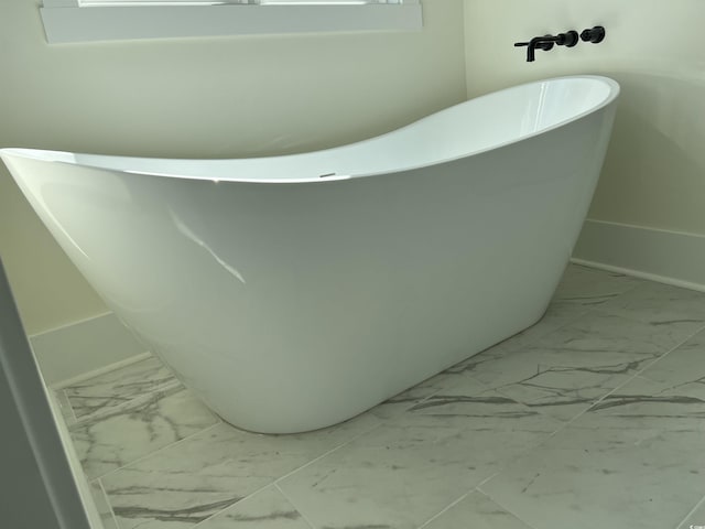 full bathroom with marble finish floor and a freestanding tub