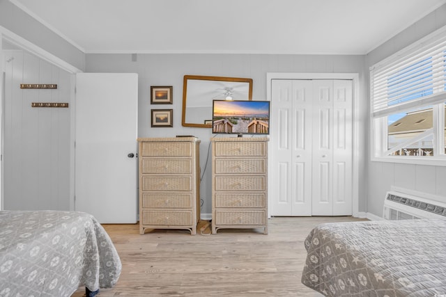 bedroom featuring light wood-type flooring, ornamental molding, an AC wall unit, a closet, and wood walls