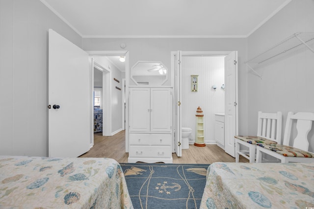 bedroom featuring light wood-type flooring, ornamental molding, wooden walls, and ensuite bath