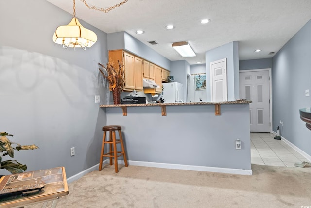 kitchen featuring a kitchen breakfast bar, light carpet, hanging light fixtures, and white refrigerator