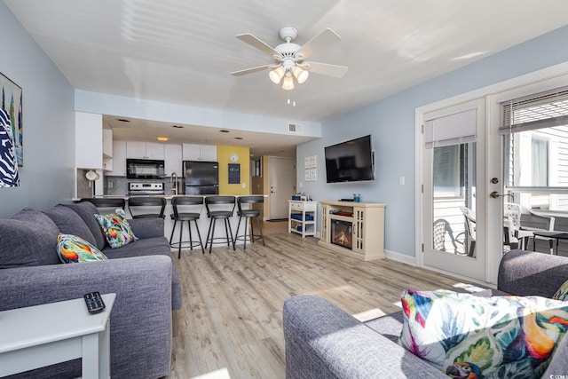 living room featuring ceiling fan, sink, and light wood-type flooring