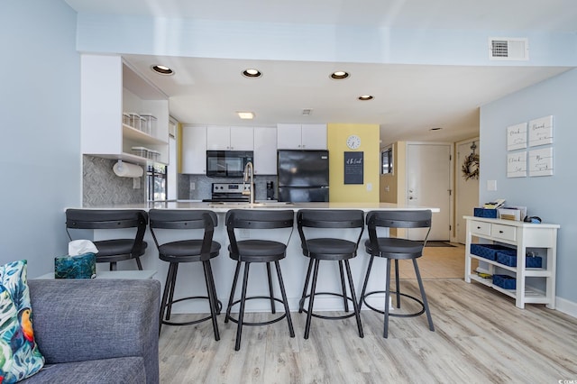 kitchen with white cabinetry, a kitchen breakfast bar, kitchen peninsula, and black appliances