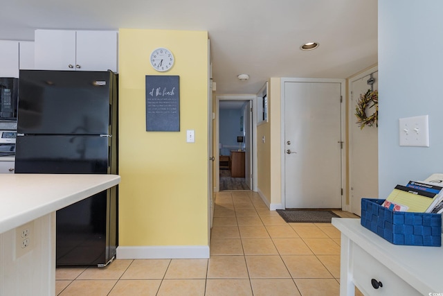 kitchen with built in microwave, light tile patterned flooring, black refrigerator, and white cabinets