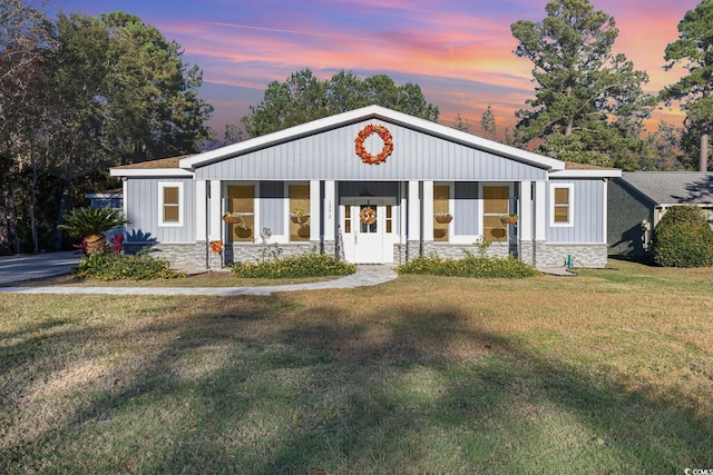 view of front of house featuring board and batten siding, stone siding, and a front lawn