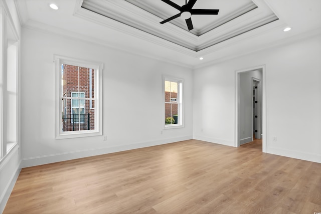 empty room with crown molding, light hardwood / wood-style flooring, ceiling fan, and a tray ceiling