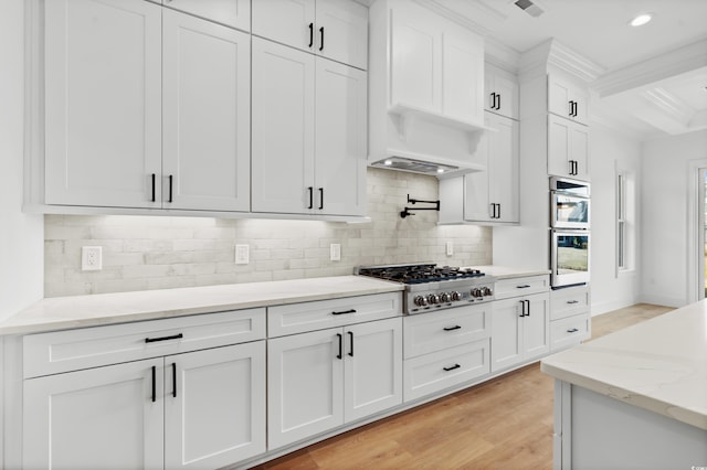 kitchen featuring appliances with stainless steel finishes, white cabinetry, backsplash, light hardwood / wood-style floors, and beam ceiling