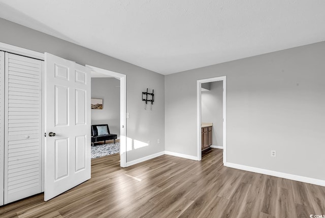 unfurnished bedroom featuring a textured ceiling, a closet, light hardwood / wood-style flooring, and ensuite bath