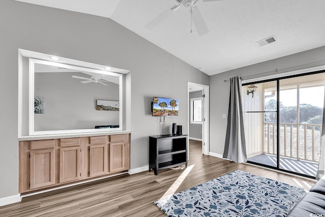 living room with a textured ceiling, ceiling fan, light hardwood / wood-style floors, and lofted ceiling