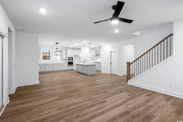 unfurnished living room featuring sink, ceiling fan with notable chandelier, and light hardwood / wood-style flooring