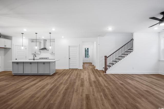 kitchen featuring a center island with sink, dark hardwood / wood-style flooring, pendant lighting, wall chimney range hood, and white cabinets