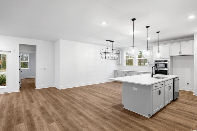 kitchen with sink, decorative light fixtures, a center island with sink, hardwood / wood-style flooring, and white cabinets