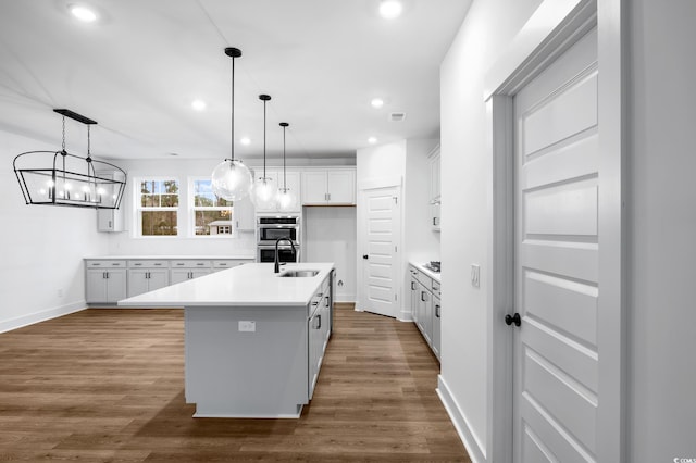 kitchen featuring white cabinetry, a center island with sink, stainless steel double oven, and decorative light fixtures