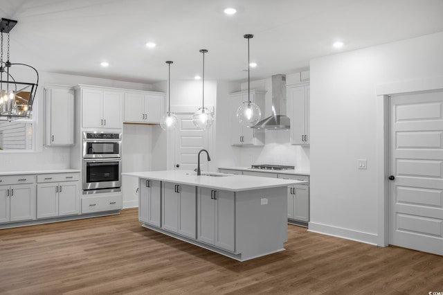 kitchen featuring pendant lighting, stainless steel appliances, a center island with sink, and wall chimney range hood